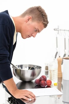 Young handsome blond man standing in the kitchen and reading recipe