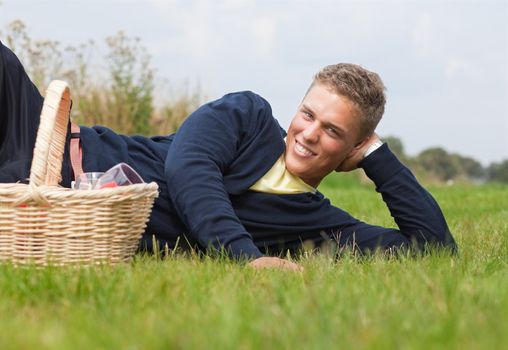 Young handsome blond lying on the grass with picnic basket
