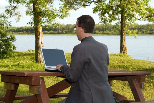 A businessman working on a laptop outside in a park