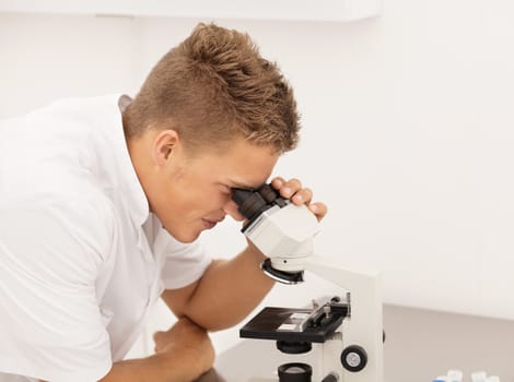 Young blond researcher concentrated on picture in his microscope