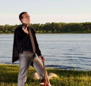 A young businessman standing by a small lake with his guitar