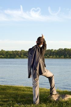 A young man wearing a business suit pointing at some clouds that say I love you