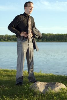 A young businessman holding his stomach at the lake, because he has a stomach ache