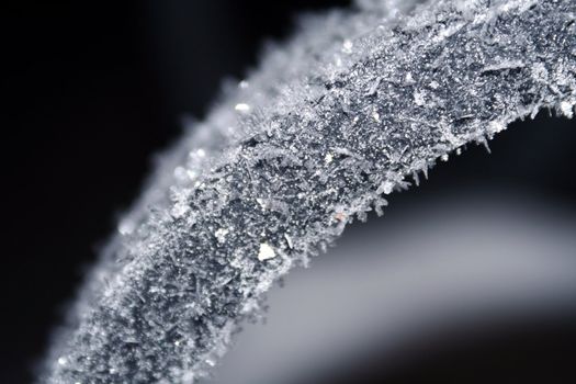 A macro image of ice crystals forming on cold black metal.