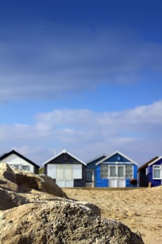 A portrait format image of blue painted wooden beach huts in soft focus to background, with sharp focus to a rock formation to front of image. Room for copy above image.