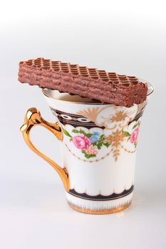 Cup with tea and a wafer covered with chocolate.