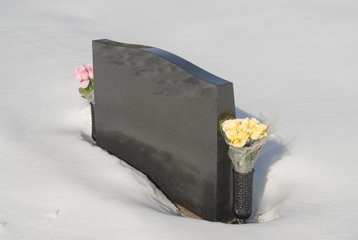 Winter grave with flowers on the side and snow on the ground