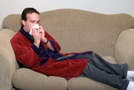 A sick man lying on a couch, blowing his nose