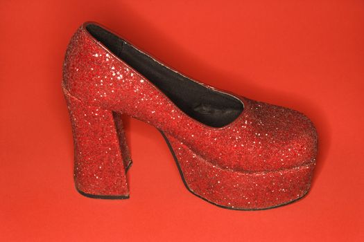 Red glitter high heel shoe against red background.