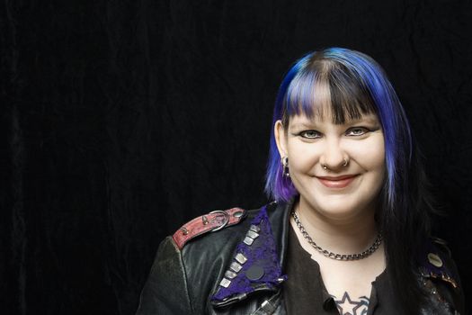 Portrait of smiling Caucasian woman with blue hair and black leather jacket against black background.