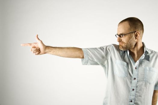 Portrait of Caucasian man holding hand out like a gun standing against white background.