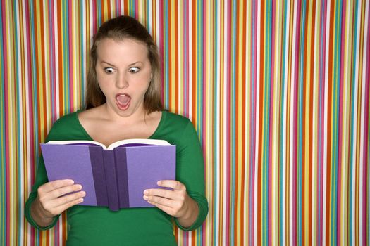 Young Caucasian female adult reading book making expression.