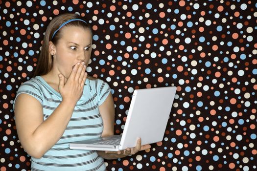 Young Caucasian woman holding laptop looking shocked.