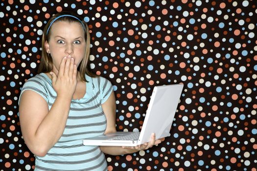 Young Caucasian woman holding laptop looking shocked.