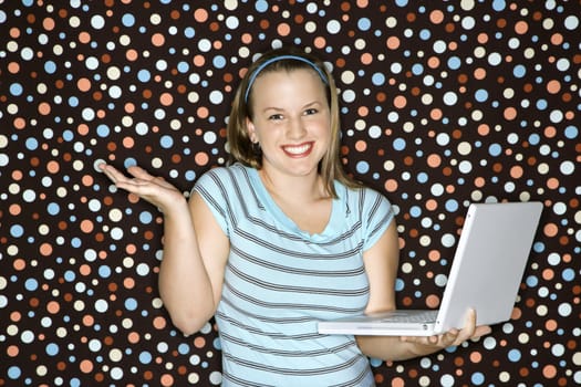 Young Caucasian woman holding laptop shrugging and smiling.