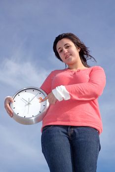 Caucasian young woman holding a big clock over blue sky