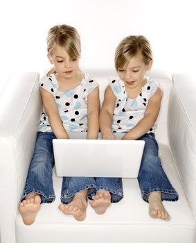 Female children Caucasian twins playing with laptop computer.