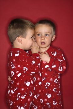 Young male twin child whispering to other twin.