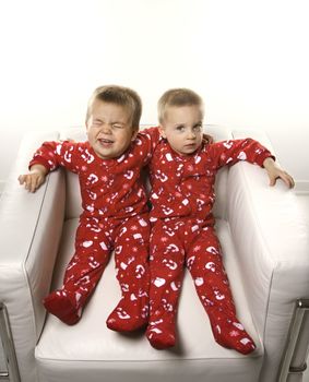 Caucasian male twin children sitting together on chair.