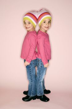 Young female twin Caucasian children standing back to back.