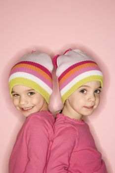 Young female twin Caucasian children standing back to back.