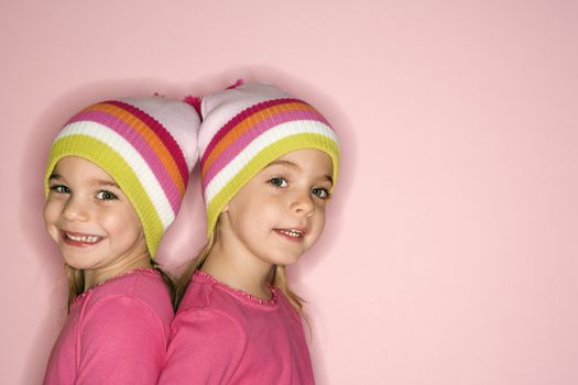 Young female twin Caucasian children standing back to back.