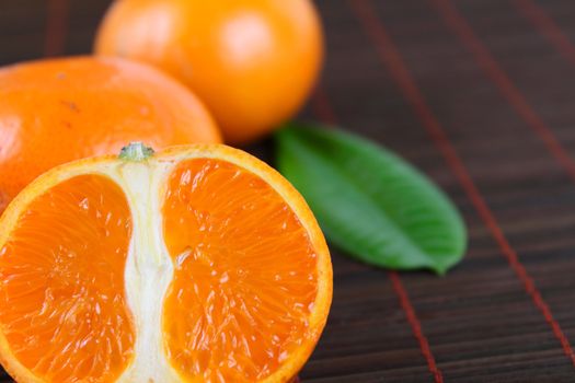 The cut tangerine against a bamboo napkin and the whole tangerine with green sheet removed close up