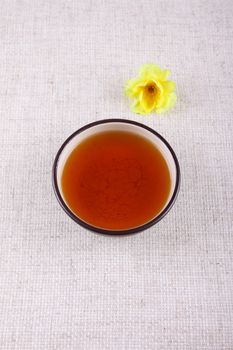 Cup of tea with a yellow flower on a linen napkin removed close up