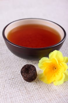 Cup of tea with a yellow flower on a linen napkin removed close up