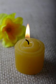 Burning candle on a linen napkin with a yellow flower on a background