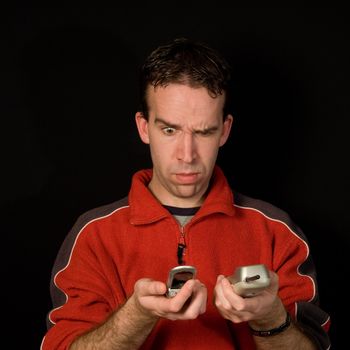 Young man comparing phones isolated against a dark background