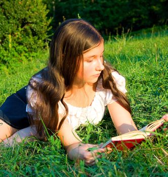 The young girl reads the book, laying on a grass