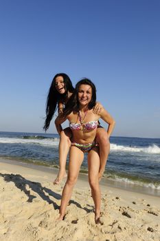 Beach fun: Girl piggybacking her friend on the beach