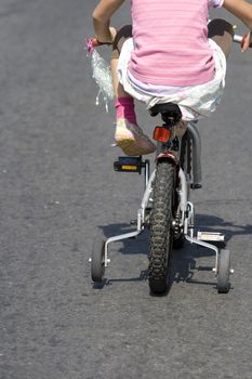 Little girl in pink learning to ride on a tricycle with training wheels
