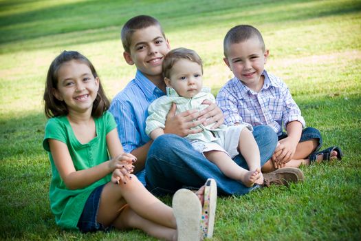 A group of four kids with one girl and three boys.  Brothers and sisters getting along nicely.  Shallow depth of field with sharp focus on the boys.