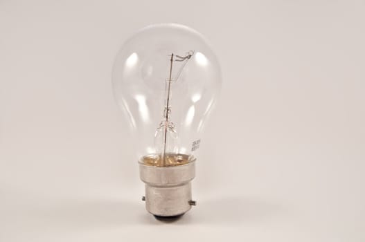 Close on an isolated clear glass light bulb arranged vertically over light grey.