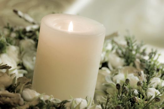 The big white candle in a wreath from artificial flowers. A wedding composition, an ornament 