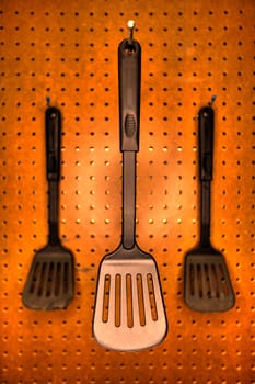 Professional cooking utensils in a restaurant kitchen, hanging o a pegboard wall.