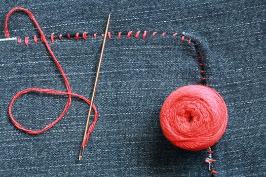 Closeup of needle and red thread on hole-ridden jeans textured