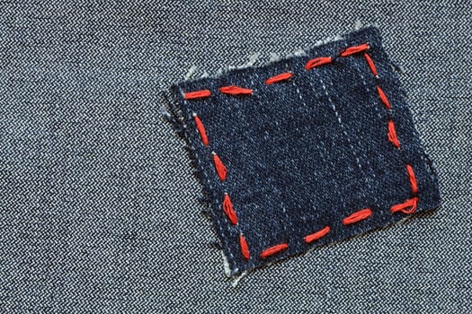 Patch with red thread attached on jeans textured