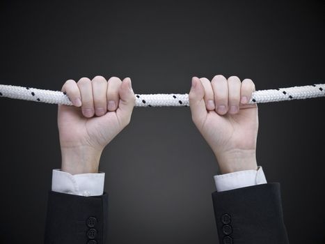 Close up on a businessman's hands hanging on a rope.