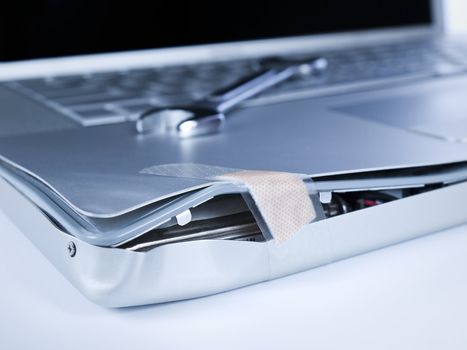 A band aid is fixing a damaged laptop. A spanner is over the computer.