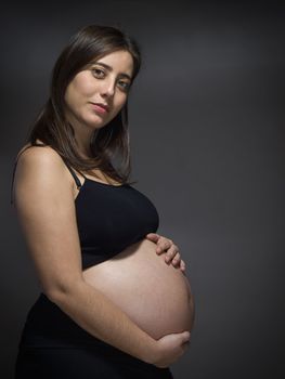 A pregnant woman holds her big belly over a gray background.