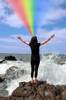 a beautiful woman doing yoga on the rocks showing a healthy way to live a happy and relaxed lifestyle in a world full of stress with a beautiful rainbow in the background
