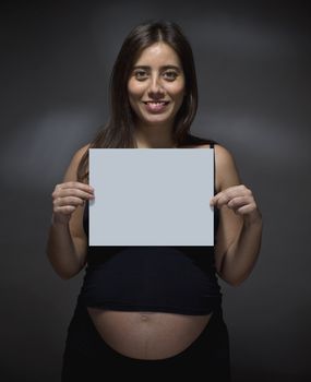 Pregnant woman holding a white card over gray background.