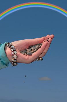 a hand full of earth against a beautiful blue sky with a rainbow in the background