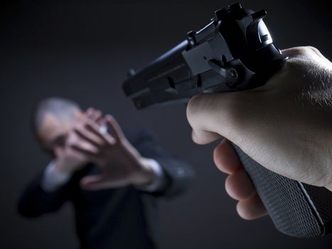 A threatening hand pointing a gun on an unarmed helpless businessman.