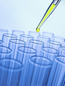 Close up of a pipette dropping a yellow sample into a test tube.