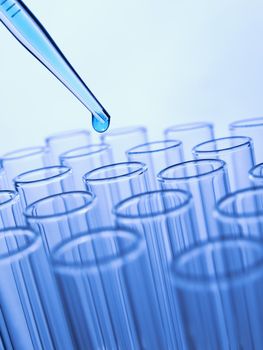 Close up of a pipette dropping a blue sample into a test tube.