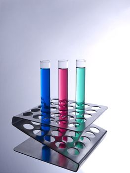 Three test tubes filled with colored liquids on a metallic rack.